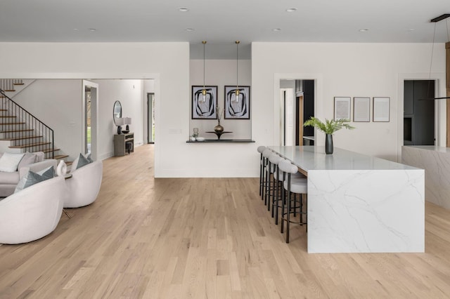 interior space featuring white cabinetry, light stone counters, a kitchen island, decorative light fixtures, and light wood-type flooring