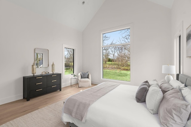 bedroom with high vaulted ceiling, light hardwood / wood-style floors, and multiple windows