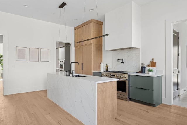 kitchen featuring high end stainless steel range, sink, light hardwood / wood-style flooring, pendant lighting, and a kitchen island with sink