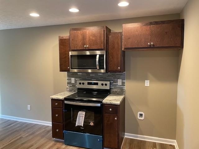 kitchen featuring backsplash, dark brown cabinets, light wood-type flooring, and appliances with stainless steel finishes