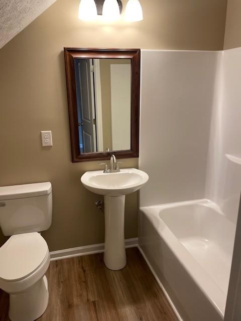 bathroom featuring hardwood / wood-style floors, a bath, toilet, and a textured ceiling