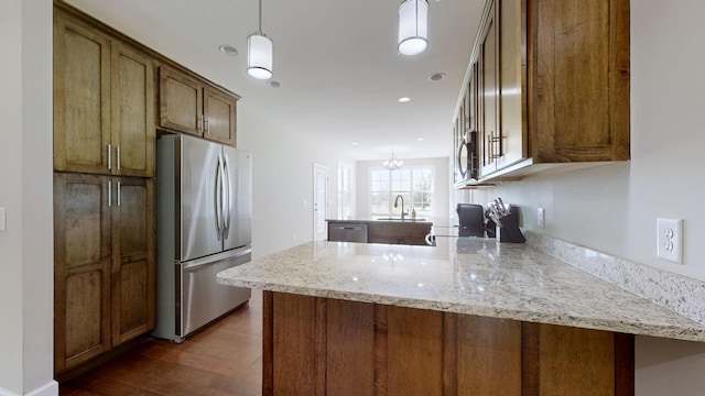 kitchen featuring kitchen peninsula, light stone counters, hanging light fixtures, and appliances with stainless steel finishes