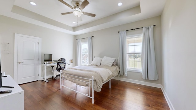 bedroom with dark hardwood / wood-style flooring, a tray ceiling, and ceiling fan