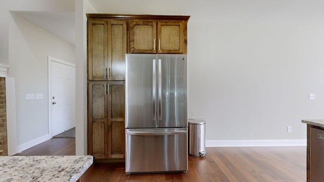 kitchen with stainless steel fridge, dark wood-type flooring, and light stone counters