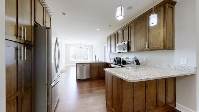 kitchen featuring kitchen peninsula, pendant lighting, stainless steel appliances, and light stone counters