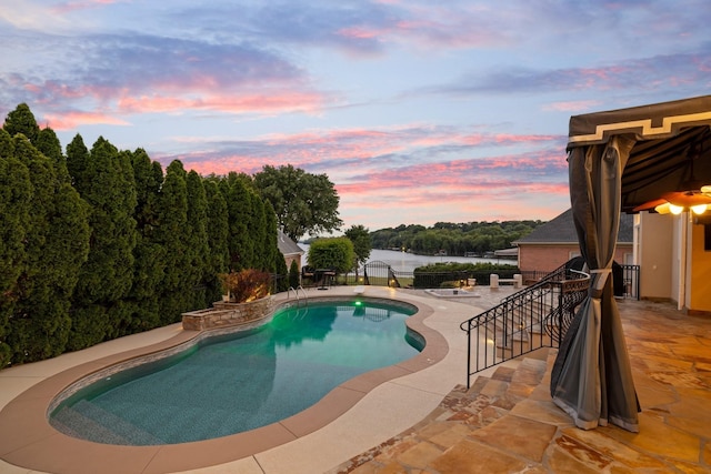 pool at dusk with a patio area and a water view