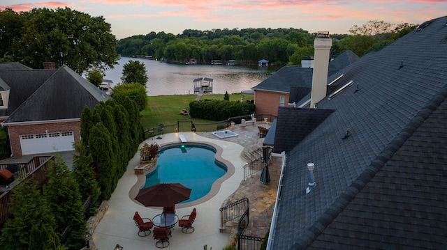 pool at dusk with a lawn, a water view, and a patio