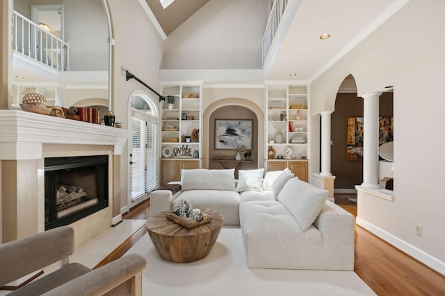 living room with crown molding, light hardwood / wood-style flooring, a high ceiling, and decorative columns