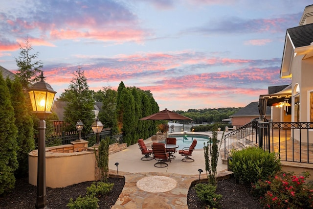 patio terrace at dusk featuring a fenced in pool