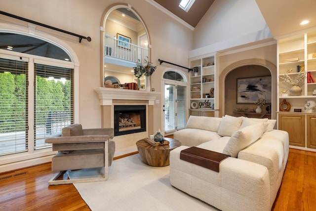 living room with built in shelves, a healthy amount of sunlight, wood-type flooring, and ornamental molding