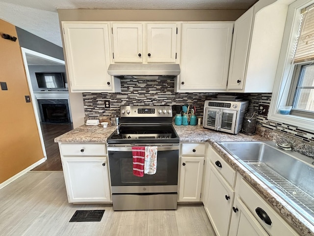 kitchen featuring white cabinetry, light hardwood / wood-style flooring, backsplash, a textured ceiling, and stainless steel stove