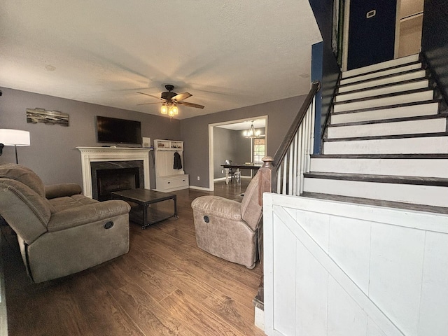 living room featuring hardwood / wood-style floors, ceiling fan with notable chandelier, a fireplace, and a textured ceiling