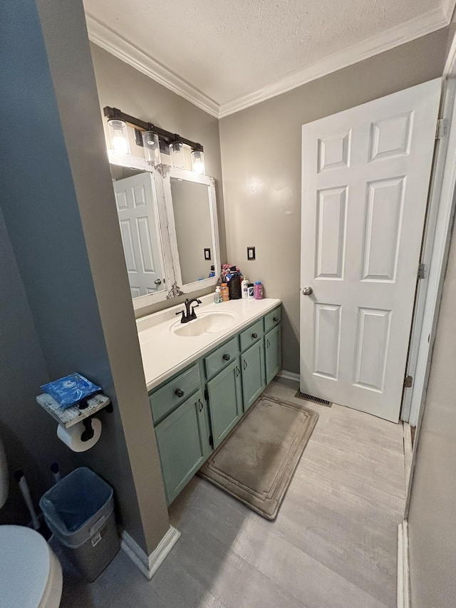 bathroom with vanity, toilet, ornamental molding, a textured ceiling, and wood-type flooring