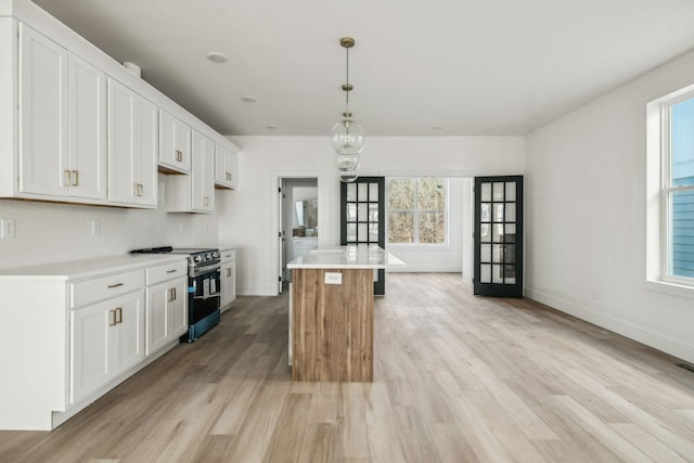 kitchen with a wealth of natural light, decorative light fixtures, white cabinets, a kitchen island, and stainless steel electric range