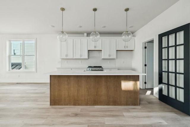 kitchen featuring white cabinets, decorative light fixtures, a kitchen island, and light hardwood / wood-style floors