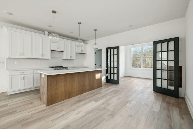 kitchen with light wood-type flooring, backsplash, a kitchen island, pendant lighting, and white cabinetry