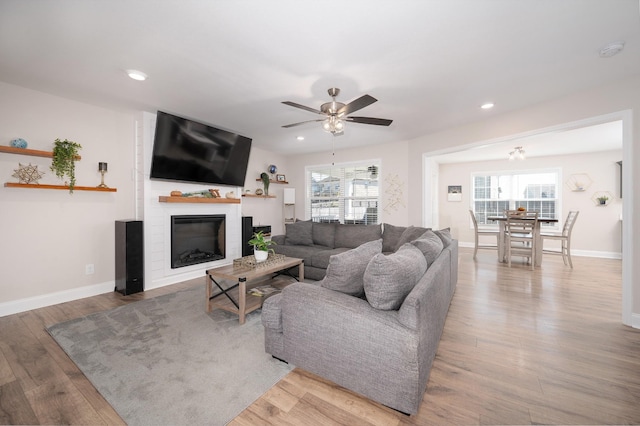 living room featuring ceiling fan, light hardwood / wood-style floors, a healthy amount of sunlight, and a fireplace