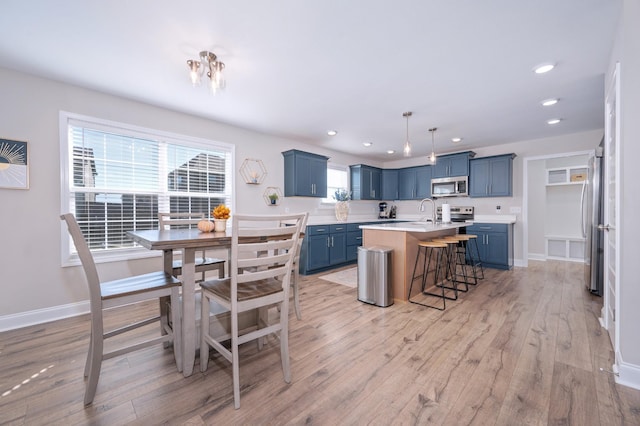 kitchen featuring a kitchen breakfast bar, stainless steel appliances, blue cabinetry, a center island with sink, and light hardwood / wood-style flooring