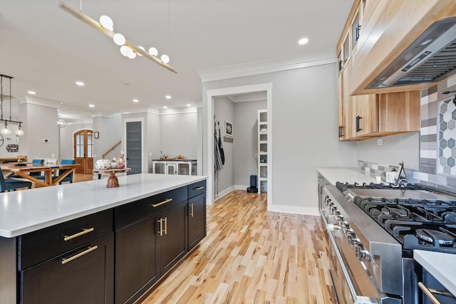 kitchen featuring light brown cabinetry, premium range hood, crown molding, pendant lighting, and light hardwood / wood-style flooring