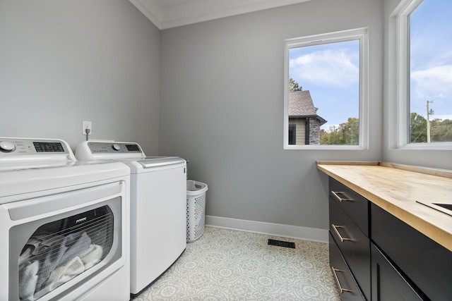 laundry room featuring washer and dryer, ornamental molding, cabinets, and a healthy amount of sunlight