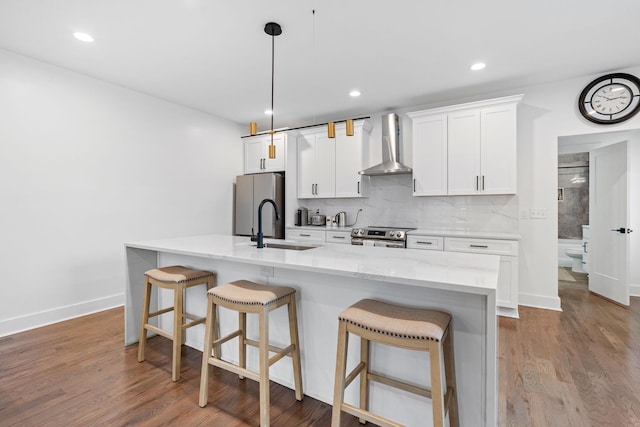 kitchen featuring sink, white cabinets, a kitchen island with sink, wall chimney range hood, and a breakfast bar