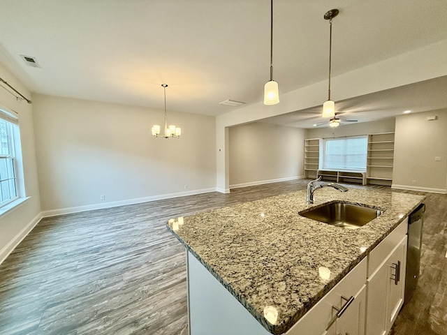 kitchen featuring pendant lighting, a center island with sink, sink, light stone countertops, and white cabinetry