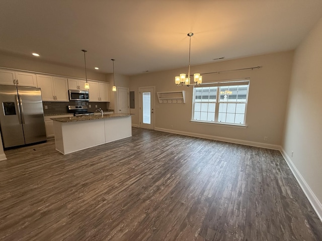 kitchen featuring a kitchen island with sink, white cabinetry, stainless steel appliances, and decorative light fixtures