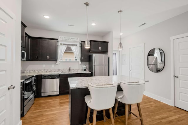 kitchen featuring a center island, stainless steel appliances, light hardwood / wood-style flooring, and hanging light fixtures