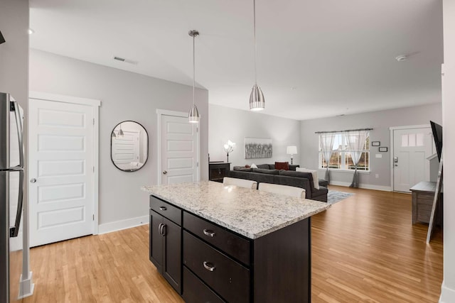 kitchen featuring light stone countertops, a kitchen island, pendant lighting, light hardwood / wood-style flooring, and stainless steel refrigerator