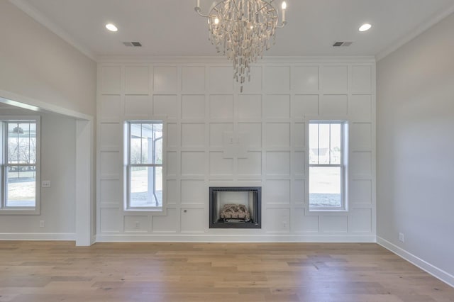 unfurnished living room with light wood-type flooring, an inviting chandelier, and crown molding