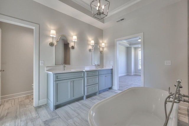 bathroom featuring a raised ceiling, a bath, a chandelier, vanity, and ornamental molding