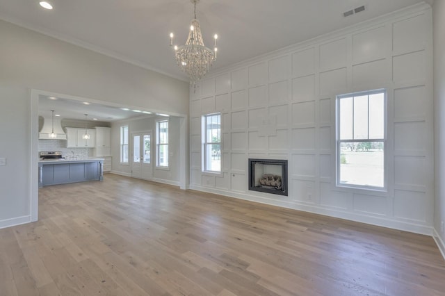 unfurnished living room featuring a chandelier, light wood-type flooring, and ornamental molding