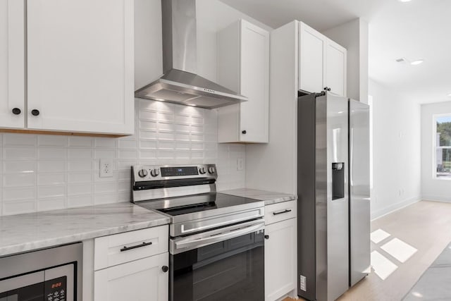 kitchen featuring light stone countertops, white cabinetry, stainless steel appliances, wall chimney range hood, and decorative backsplash