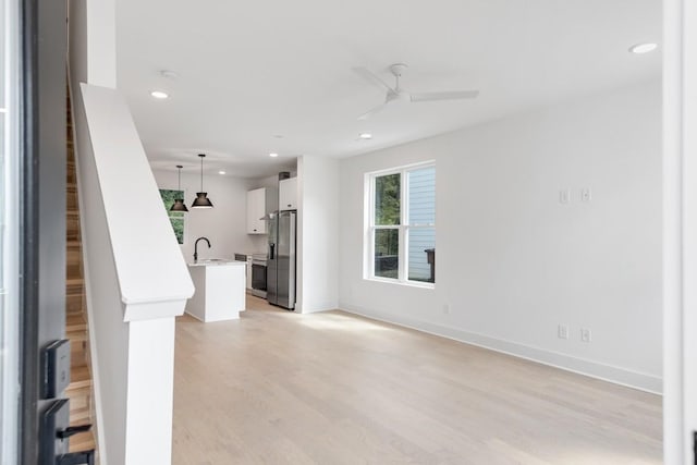 unfurnished living room featuring light hardwood / wood-style flooring, ceiling fan, and sink