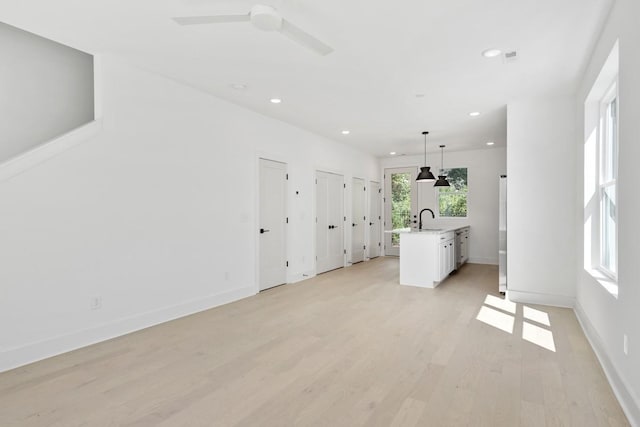 unfurnished living room with ceiling fan, sink, and light hardwood / wood-style floors