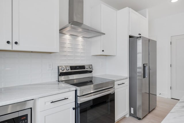 kitchen featuring white cabinetry, light stone countertops, wall chimney range hood, appliances with stainless steel finishes, and light wood-type flooring