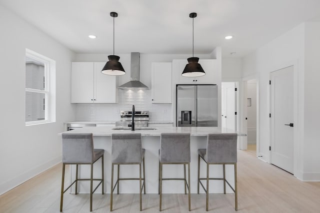 kitchen featuring stainless steel fridge with ice dispenser, white cabinetry, a kitchen island with sink, and wall chimney exhaust hood