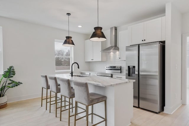 kitchen with appliances with stainless steel finishes, sink, wall chimney range hood, a center island with sink, and white cabinets