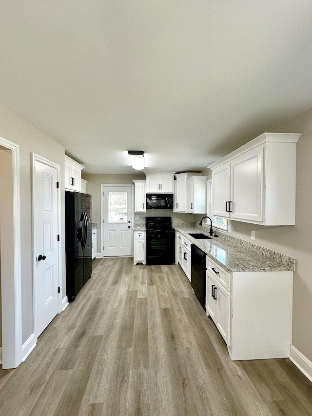 kitchen with black appliances, white cabinets, sink, light hardwood / wood-style flooring, and light stone countertops