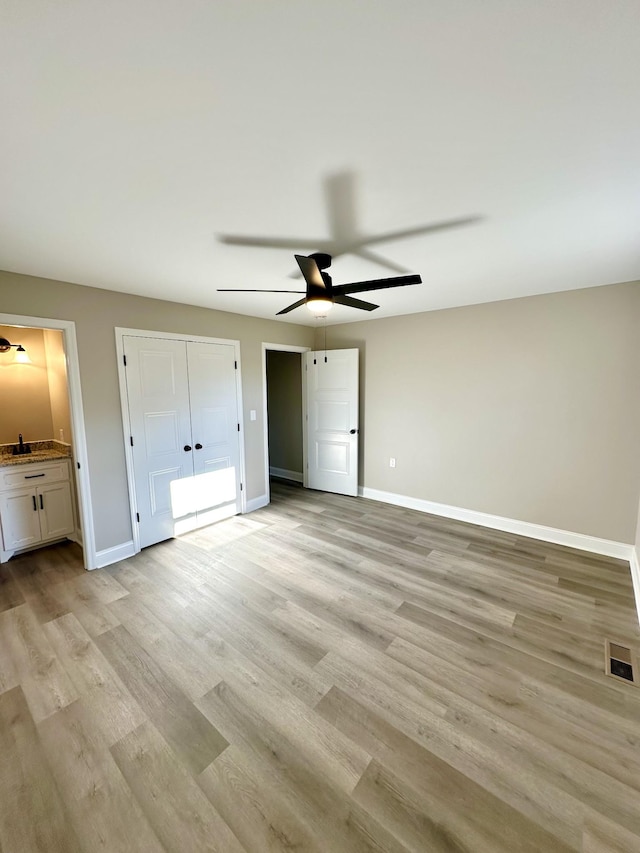 unfurnished bedroom with connected bathroom, ceiling fan, sink, and light wood-type flooring