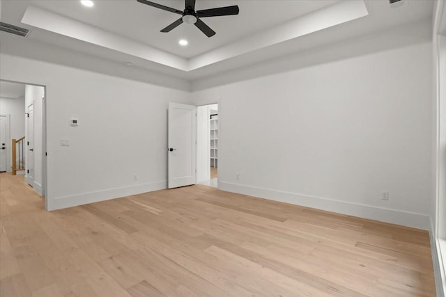 spare room featuring a tray ceiling, ceiling fan, and light hardwood / wood-style flooring