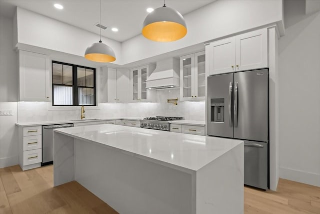 kitchen with decorative light fixtures, a center island, custom range hood, stainless steel appliances, and white cabinets