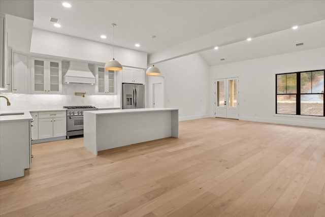 kitchen featuring wall chimney range hood, sink, white cabinetry, stainless steel appliances, and a kitchen island