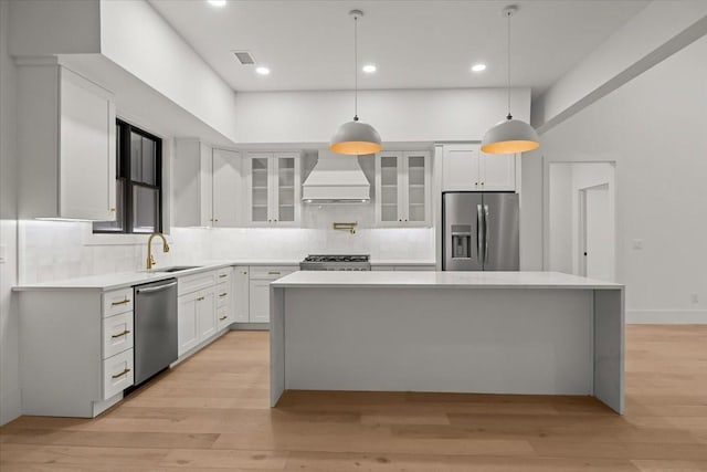 kitchen featuring pendant lighting, sink, white cabinets, stainless steel appliances, and custom range hood