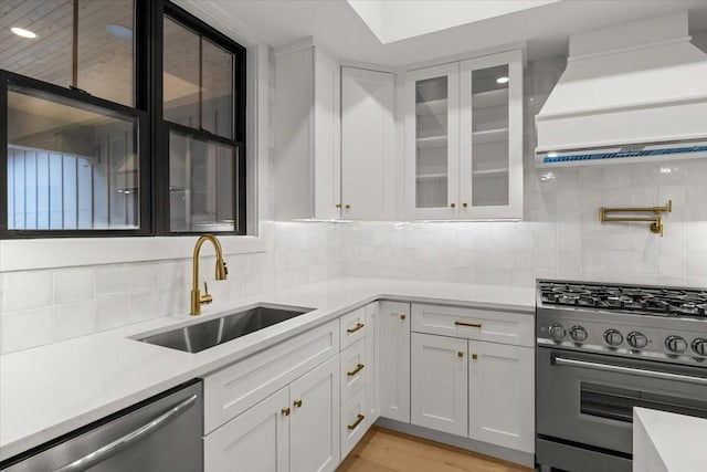 kitchen featuring appliances with stainless steel finishes, white cabinetry, sink, decorative backsplash, and custom range hood