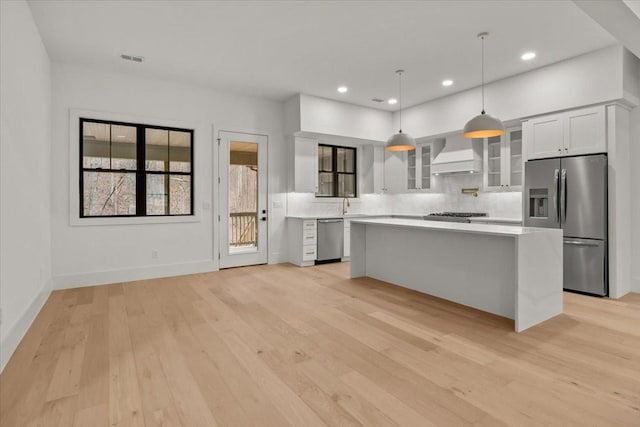 kitchen with wall chimney range hood, appliances with stainless steel finishes, white cabinetry, a center island, and decorative light fixtures