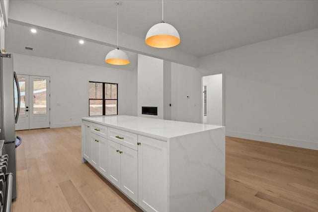 kitchen featuring stainless steel refrigerator, white cabinetry, hanging light fixtures, a kitchen island, and light wood-type flooring