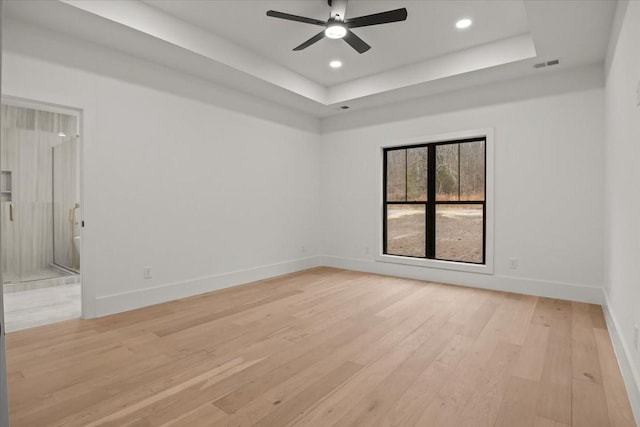 spare room featuring a tray ceiling, ceiling fan, and light wood-type flooring