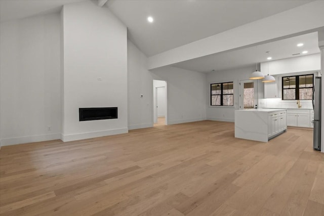 unfurnished living room with beam ceiling, light hardwood / wood-style flooring, and high vaulted ceiling