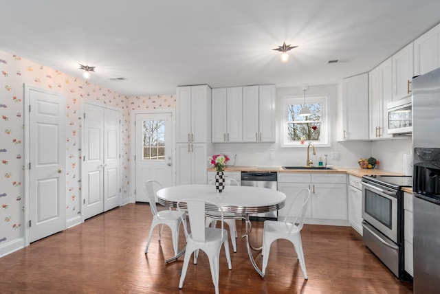 kitchen with sink, hanging light fixtures, wood-type flooring, white cabinets, and appliances with stainless steel finishes